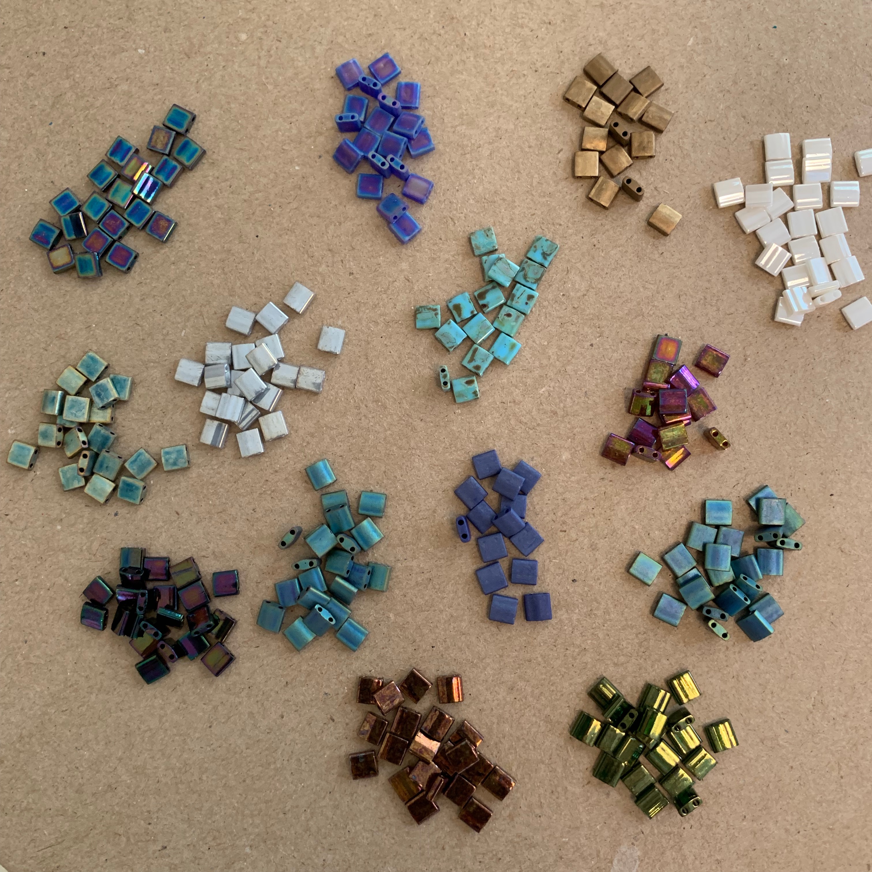 Organized piles of small, square beads, arranged by color.
